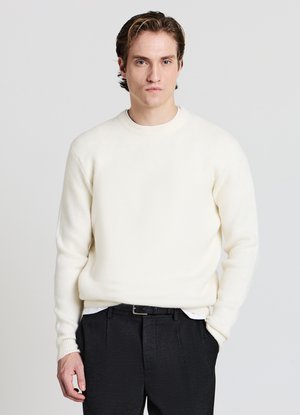 Maglione bianco lavorato a maglia con scollo rotondo e polsini a coste, indossato sopra una camicia bianca, abbinato a pantaloni eleganti neri. Tessuto liscio.