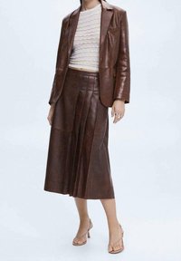 Bruine leren blazer in combinatie met een bijpassende geplooide rok, met een lichtgewicht tricot top. De outfit heeft een soepele textuur en een getailleerde pasvorm.