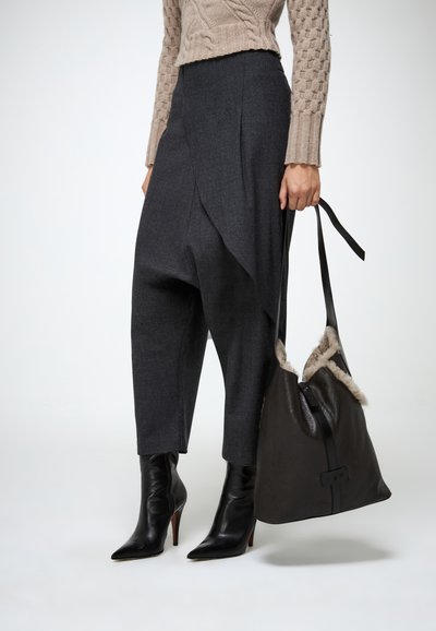 Pantalones grises ajustados con un diseño drapeado, combinados con un suéter beige de canalé y botas negras de puntera afilada. Bolso de cuero oscuro con borde de piel.