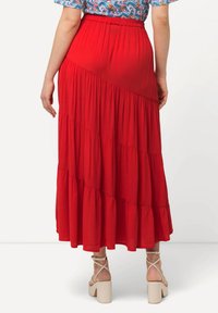 Gonna maxi rossa con un design a strati e una texture fluida, una vita elastica e un colore uniforme. Abbinata a sandali con tacco a blocco di colore chiaro.