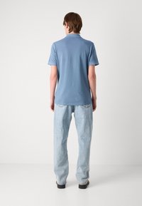 Błękitna koszulka polo z krótkim rękawem i małym kołnierzykiem, wykonana z lekkiego materiału, w zestawie z jasnoniebieskimi prostymi jeansami.