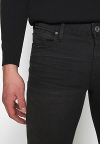 Svarta jeans i denim med smal passform, femficksdesign, metallknapp och dragkedja samt subtila blekningsdetaljer på tygstrukturen.