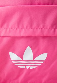 Rožinis audinys, ant kurio pavaizduotas logotipas su trimis lapų formomis ir trimis horizontaliomis baltomis juostelėmis. Audinys atrodo kaip patvari, sintetinė medžiaga.