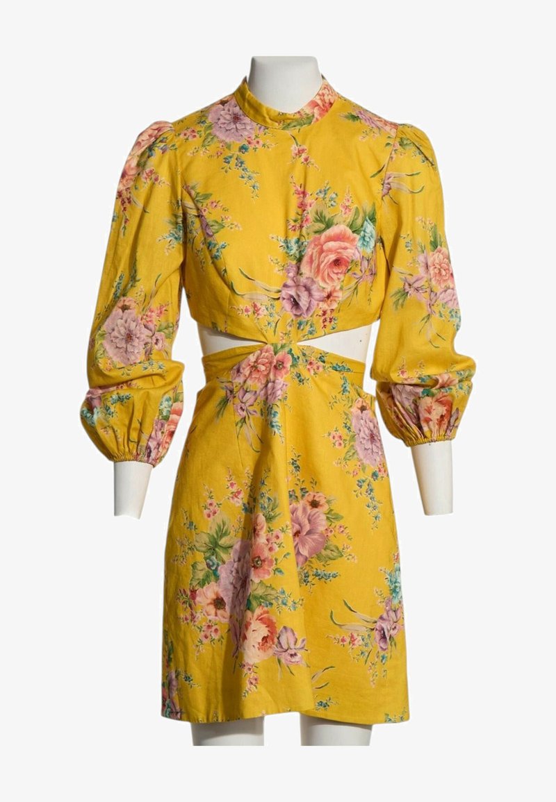 Robe fleurie jaune avec manches longues bouffantes, taille découpée et motifs floraux roses et violets sur le tissu.
