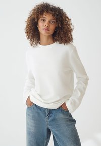 Felpa bianca a girocollo realizzata in tessuto morbido, con maniche lunghe e vestibilità comoda, abbinata a jeans in denim azzurro chiaro.