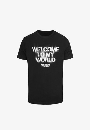 Must t-särk mustast puuvillast, millel on valge graafiline trükk, mis ütleb "TERE TULEMA MINU MAAILMA" ja "TUNDMATUD ASJAD" julge fondiga.