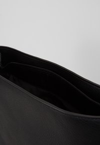 Borsa in pelle nera con tasca interna zip visibile e superficie esterna liscia su uno sfondo grigio semplice.