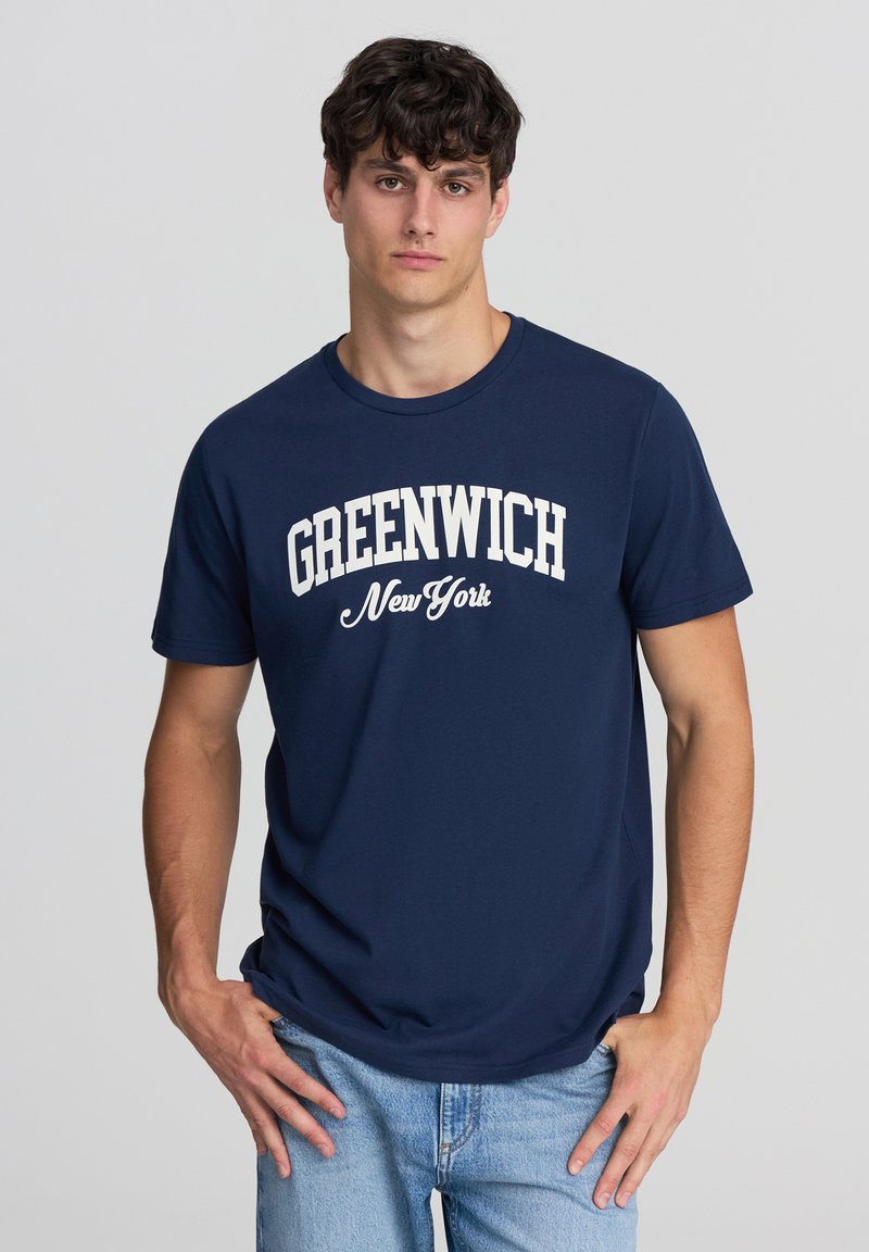 T-shirt in cotone navy con testo "GREENWICH New York" in bianco, design a collo giro, maniche corte e vestibilità rilassata. Jeans in denim opzionali.