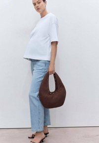 Camiseta blanca de gran tamaño, jeans rectos de mezclilla azul claro y un bolso curvado marrón con acentos metálicos, combinados con sandalias de tacón negras.