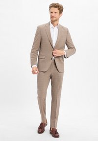 Hellbrauner karierter Anzug mit tailliertem Schnitt, kombiniert mit einem weißen Hemd. Braune Loafer runden den Look ab. Strukturierter Stoff und durchdachtes Design.