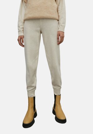 Hellbeige Strickpullover über cremfarbenen Jogginghosen, mit gerippten Bündchen. Kombiniert mit gelben Knöchelboots mit schwarzen Seitenpaneelen.