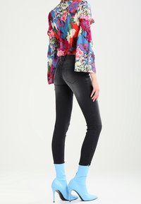 Blusa floral colorida con mangas abullonadas, combinada con jeans skinny negros y botines de tacón alto azul claro.