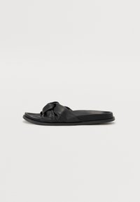 Black slide sandals made of soft leather with a knotted strap design. Flat sole, smooth texture, and minimalist style.