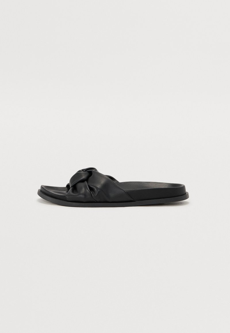Black slide sandals made of soft leather with a knotted strap design. Flat sole, smooth texture, and minimalist style.
