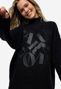 Übergroßer schwarzer Strickpullover mit einem strukturierten, glänzenden Grafikdesign. Der Stoff ist weich und hat einen gerippten Halsausschnitt und Bündchen.