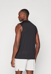 Camiseta deportiva sin mangas negra de tejido ligero, con cuello redondo y un corte holgado, combinada con pantalones cortos de color claro.