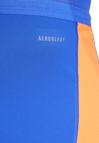 Blauwe sportieve shorts met een oranje paneel, gemaakt van gladde, lichte stof. Bevat het "AEROREADY" logo in zilver aan de linkerkant.