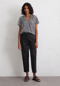 Black and white patterned short-sleeve blouse paired with black cropped trousers and black sandals. Smooth fabric, relaxed fit, and V-neck design.