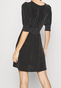 Svart klänning i kort modell med en texturerad tyg som har glittrande detaljer. Puffärmar och en figurnära midja skapar en utfläkt silhuett.