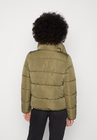 Olivgrön vadderad jacka med hög krage, sydda horisontella sömmar, långa ärmar och en mjuk, blank yta.