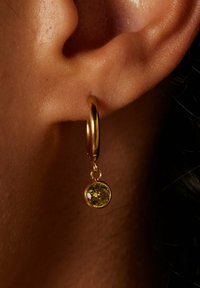 Goldene Creolen mit einem hängenden runden gelben Edelstein, ausgestattet mit einer glänzenden Oberfläche und einer glatten Textur.