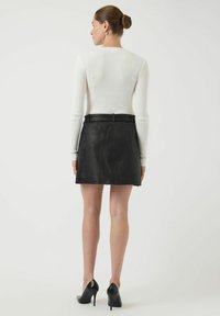 Svart lærskjørt med en tettsittende design og beltesløyfer. Modellen har på seg en hvit ribbestrikket langermet topp og svarte høye hæler.