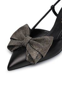 Scarpa nera con punta a punta, dal design elegante, caratterizzata da un grande fiocco metallico testurizzato sul davanti e da una sottile cinghia alla caviglia.