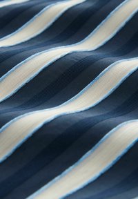Gestreifter Stoff mit abwechselnden marineblauen und cremefarbenen Wellen sowie hellblauen Akzenten, der eine strukturierte Oberfläche aufweist.