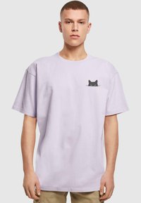 Lavender cotton t-shirt with short sleeves and a loose fit. Features a black cat graphic on the left chest pocket area.