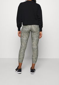 Sweatshirt noir surdimensionné, leggings ajustés à imprimé animalier vert et blanc, et chaussures de sport noires ; texture lisse et coupe ajustée.
