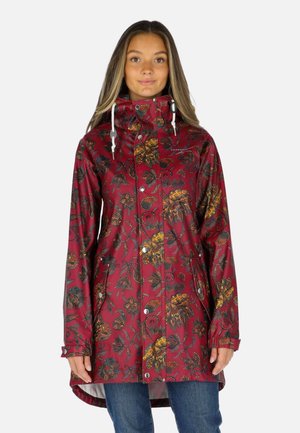 Moteris dėvi bordo spalvos neperšlampamą paltą su oranžiniais ir žaliais gėlių raštais, su sagomis priekyje ir baltais raišteliais gobtuvui.