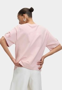 Ljusrosa, oversized T-shirt med korta ärmar. Har texturerade detaljer på ärmarna. Mjuk tygkvalitet och avslappnad passform. Bakvy.