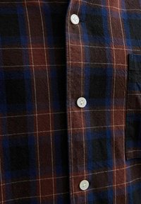 Kariertes Hemd in einem Farbschema aus Braun, Navyblau und Schwarz. Verfügt über eine Knopfschließe und eine weiche Textur, mit ausgeprägten Karomustern.