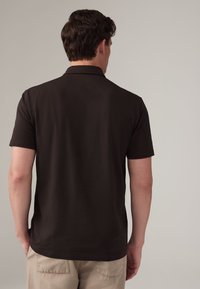 Polo nero con maniche corte, realizzato in tessuto liscio. Presenta un colletto classico e un design semplice, visto da dietro.