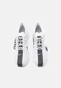 Zapatillas deportivas blancas con acentos negros, parte superior de malla, tejido texturizado, punta redonda y cordones planos; cuenta con un pequeño logo y detalles con patrón.