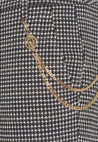 Sort-hvid houndstooth mønsteret stof med en gylden kæde detalje, der har en cirkulær metalaccent. Tekstureret og struktureret design.