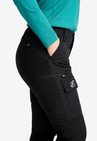 Svarta cargo-byxor med en åtsittande design, försedda med dragkedjefickor och en synlig varumärkeslapp på sidan. Tillverkade av slitstarkt material.