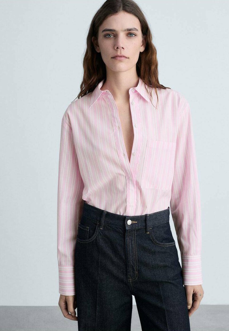 Camicia button-up a strisce rosa chiaro con maniche lunghe e taschino sul petto, abbinata a jeans in denim blu scuro. Tessuto dalla superficie liscia.