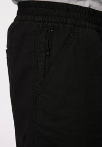 Černé šortky vyrobené z lehkého materiálu, s boční kapsou na zip, elastickým pasem a šikmým švem pro přidaný designový prvek.