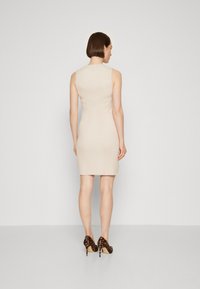 Robe beige côtelée avec une silhouette ajustée, sans manches et un petit accent rond au dos. Associée à des talons hauts à imprimé léopard.
