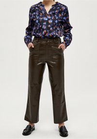 Blå och orange mönstrad blus med V-ringning, paret med högmidjade, mörkbruna läderbyxor och svarta loafers.