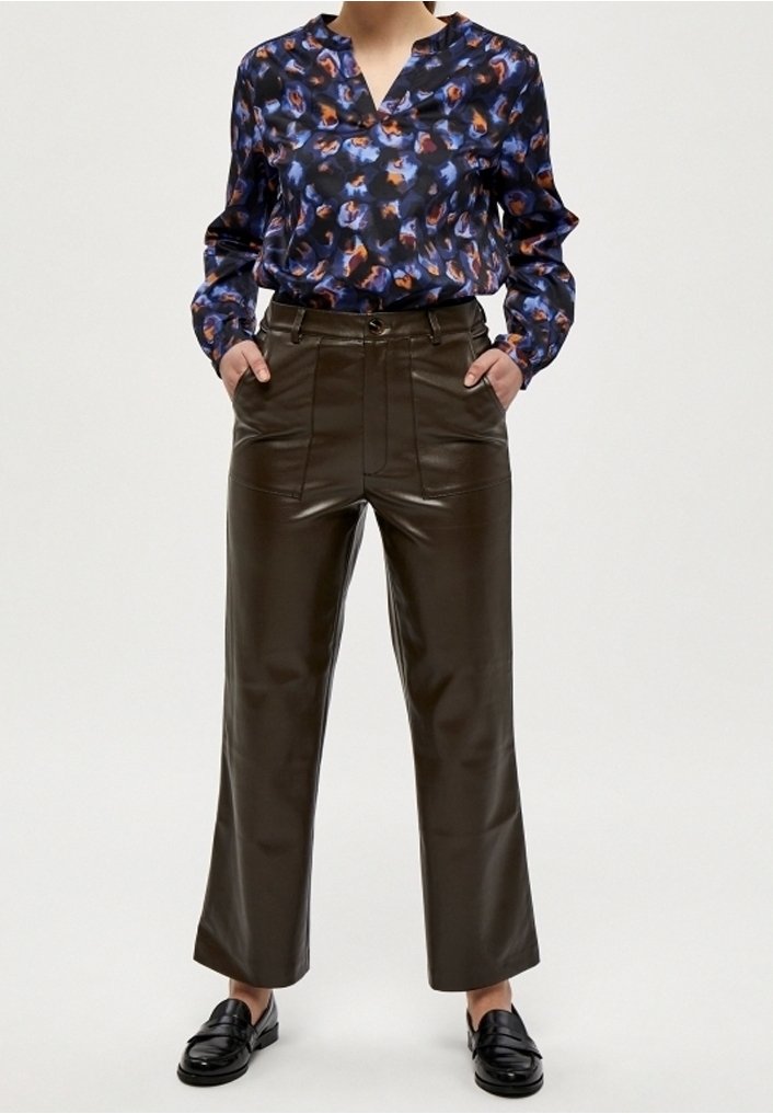 Blå och orange mönstrad blus med V-ringning, paret med högmidjade, mörkbruna läderbyxor och svarta loafers.