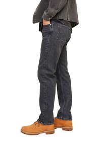 Juodos denim kelnės tiesaus kirpimo, minimalus dėvėjimasis, penkios kišenės ir sidabrinės detalės. Dėvimos su rudos spalvos batais.
