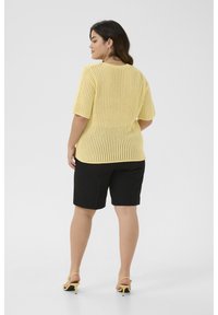 Haut en tricot jaune à manches courtes avec un motif en mailles ouvertes associé à un short noir. Les détails notables incluent un col rond et une finition texturée.
