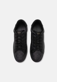 Black sneakers with a textured pattern, featuring black laces and stitched accents. Coach logo in gold on the tongue. Rubber sole.