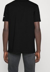 Black cotton t-shirt featuring a crew neckline and short sleeves. Back view shows a plain design with no patterns or accents.