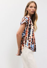 Vrh z kratkimi rokavi v vzorcu tie-dye z odtenki oranžne, modre in črne barve. Mehka tkanina, okrogel izrez in ukrivljen rob.