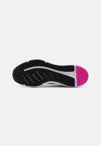 Semelle de chaussure de sport noire et rose avec une accroche texturée, présentant une rayure blanche ondulée et des motifs segmentés sur la surface pour une traction.