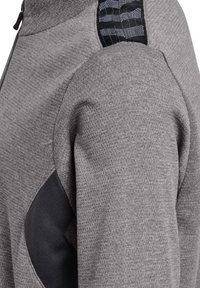 Gråt tekstureret jakkeærme med sort mesh ventilationspanel og mønstret sort lap nær skulderen.