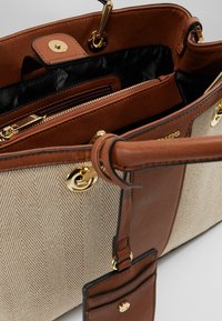 Bežová a hnědá kabelka s vzorem herringbone, zlaté kovové doplňky, více vnitřních kapsiček a odnímatelná visačka. Hladká kožená ozdoba.